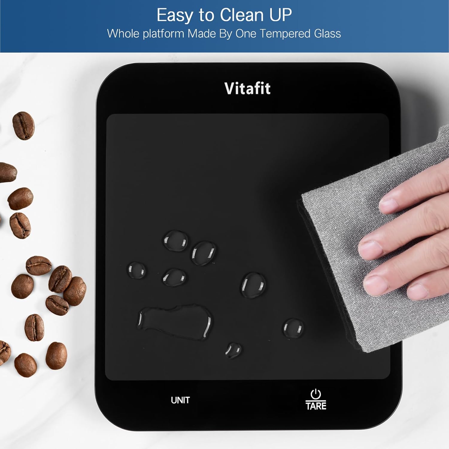 Vitafit digital kitchen scale with tempered glass platform being cleaned with microfiber cloth, surrounded by scattered coffee beans, highlighting easy cleanup feature.