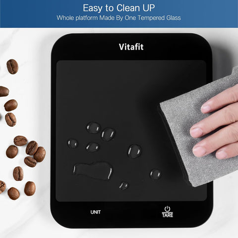 Vitafit digital kitchen scale with tempered glass platform being cleaned with microfiber cloth, surrounded by scattered coffee beans, highlighting easy cleanup feature.
