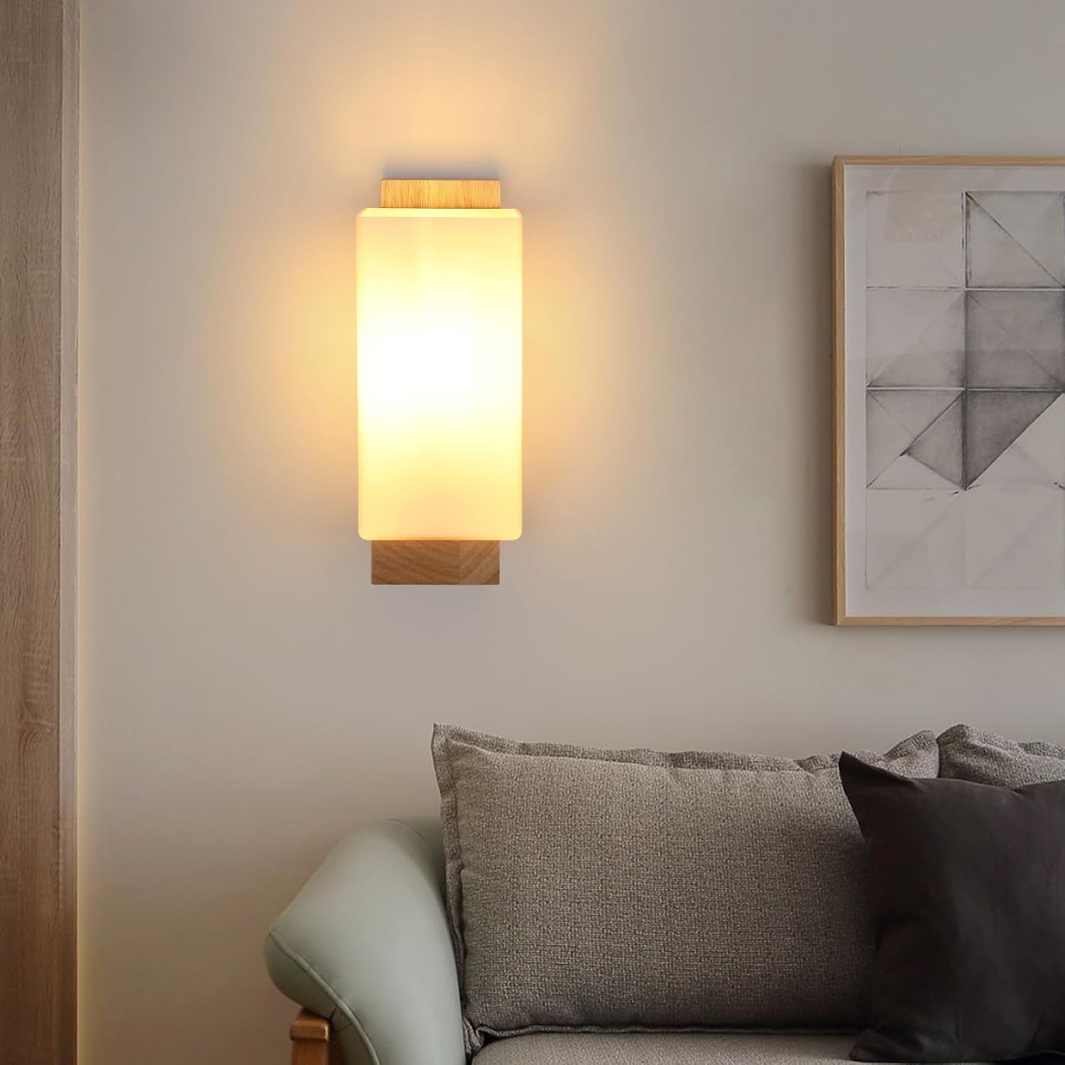 Wall-mounted lamp casting a warm glow in a living room setting with a sofa and framed picture.