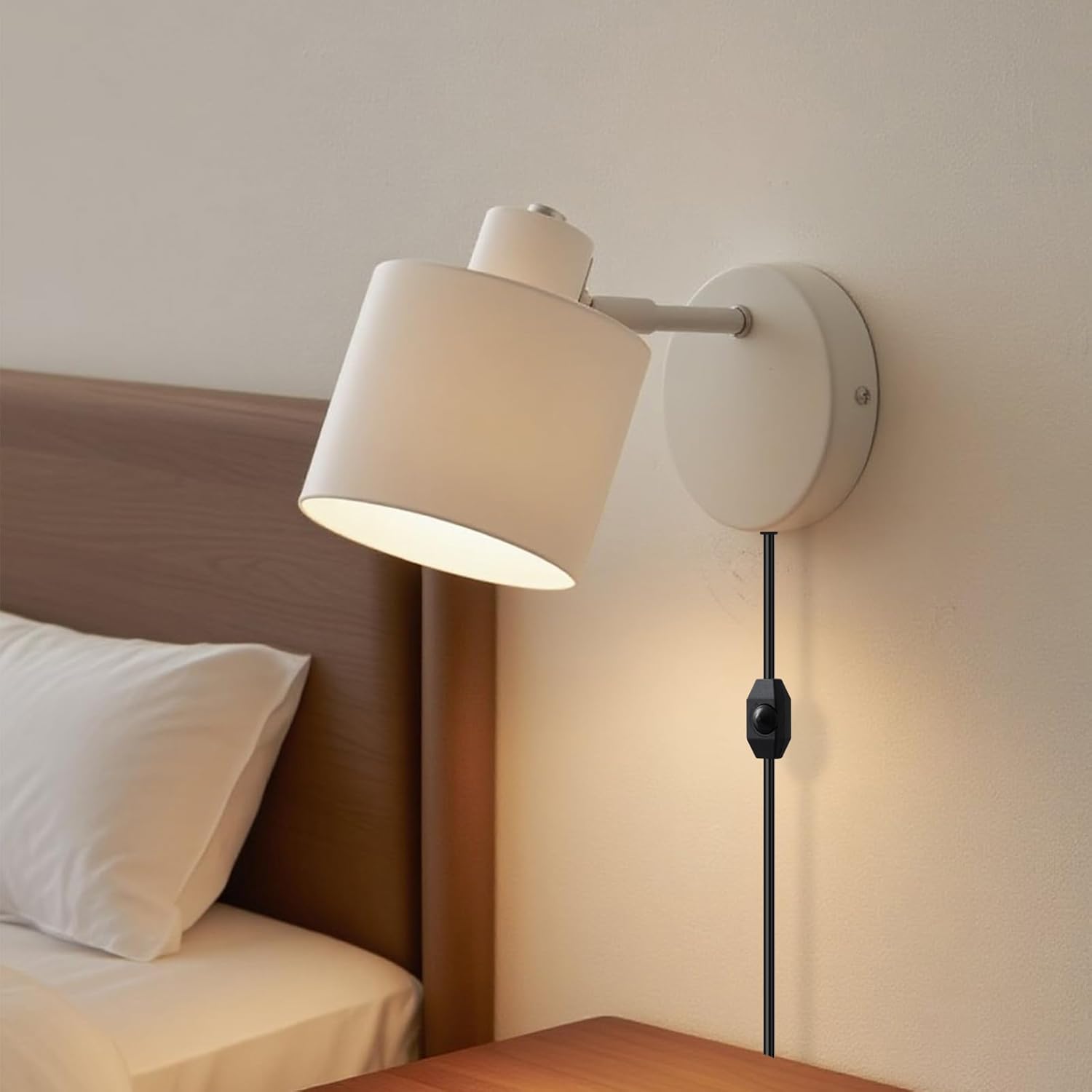 Wall-mounted lamp with beige shade on a neutral wall next to a bed.