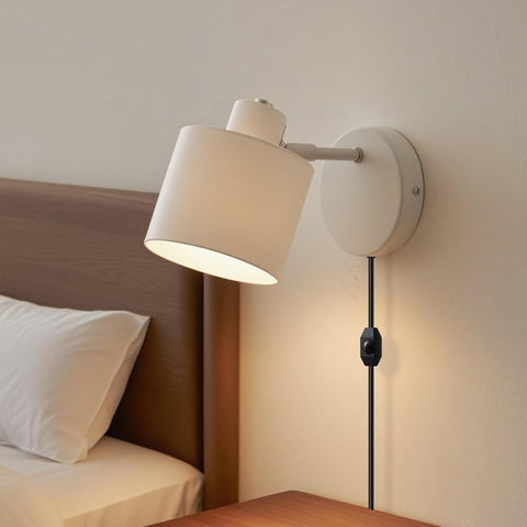Wall-mounted lamp with beige shade on a neutral wall next to a bed.