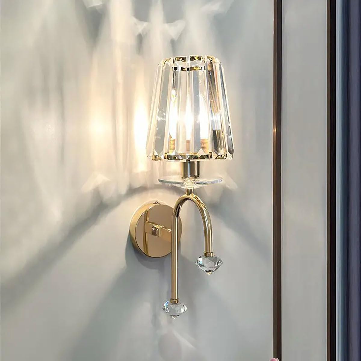 Wall-mounted lamp with gold fixture and clear glass shade on a light gray wall.