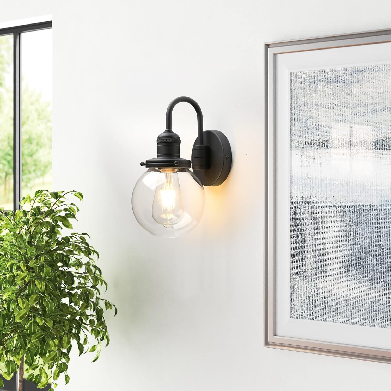 Wall-mounted light fixture on a white wall with a plant and framed picture.