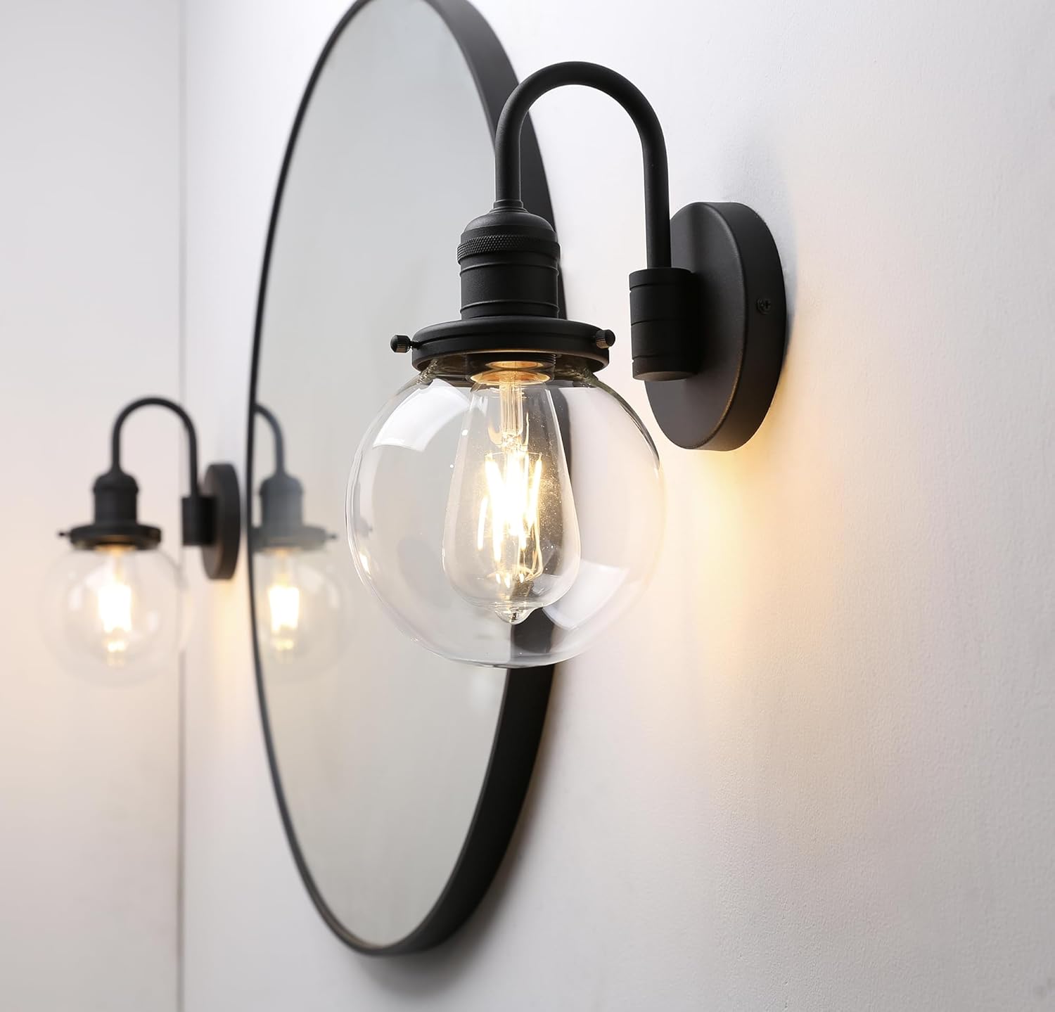 Wall-mounted light fixture with clear glass shade and black metal frame on a white wall.