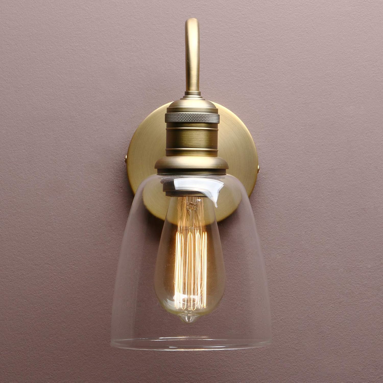 Wall-mounted light fixture with gold finish and clear glass shade on a purple wall.
