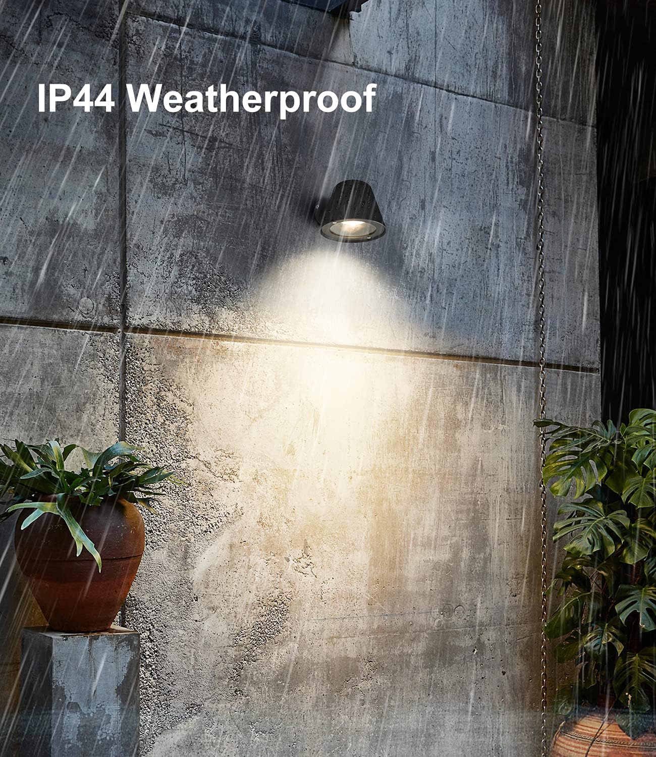 Weatherproof outdoor light fixture on a concrete wall with plants around.