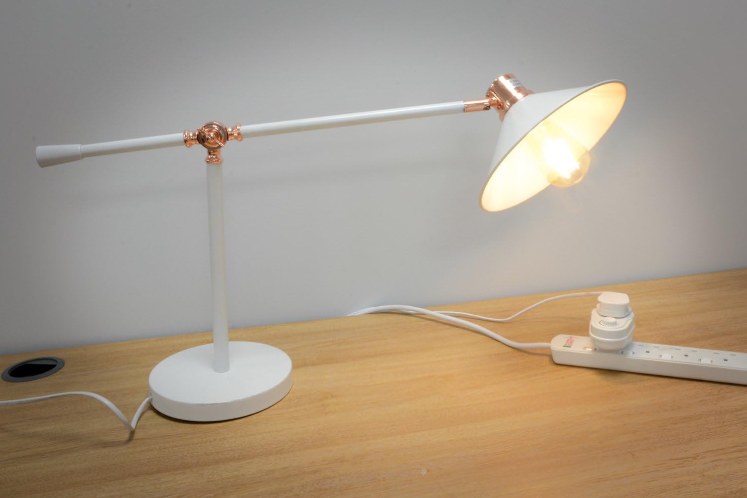 White desk lamp with copper accents on a wooden surface.