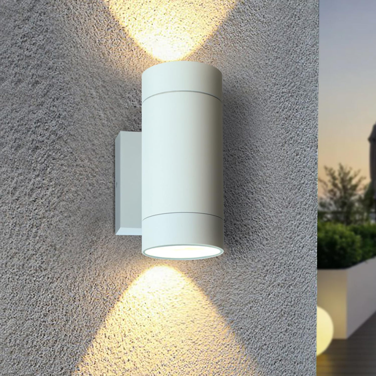White outdoor wall light fixture on a textured gray wall with a scenic background.