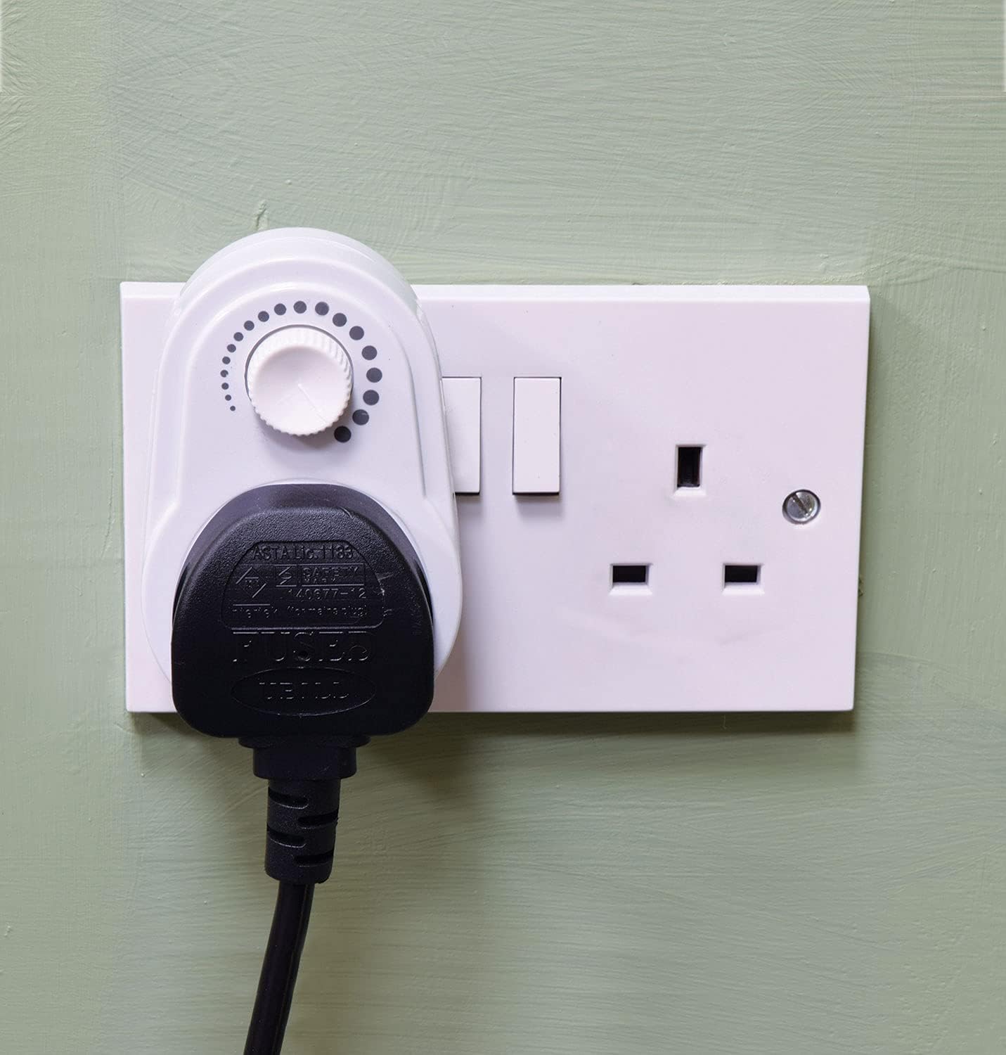 White power strip with a black plug inserted into a wall socket on a green wall.