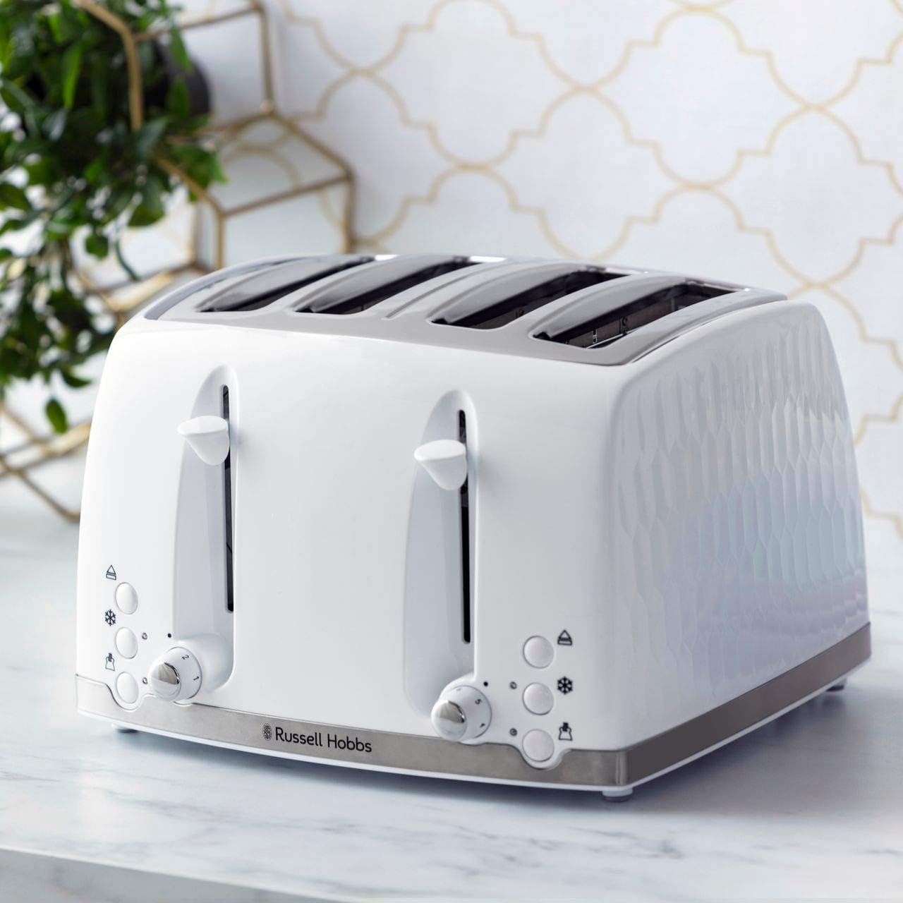 White toaster with a textured finish on a marble surface with a geometric-patterned wall in the background.