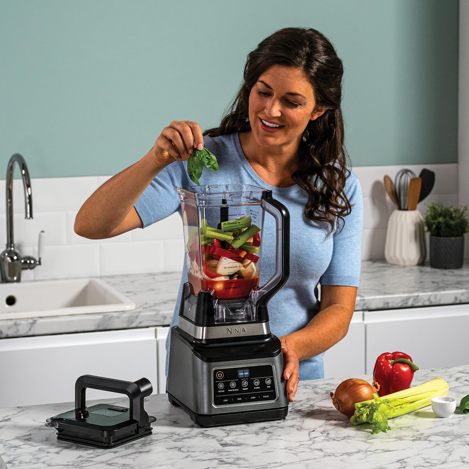 Woman adding ingredients to a Ninja blender in a kitchen.