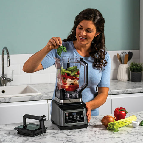 Woman adding ingredients to a Ninja blender in a kitchen.