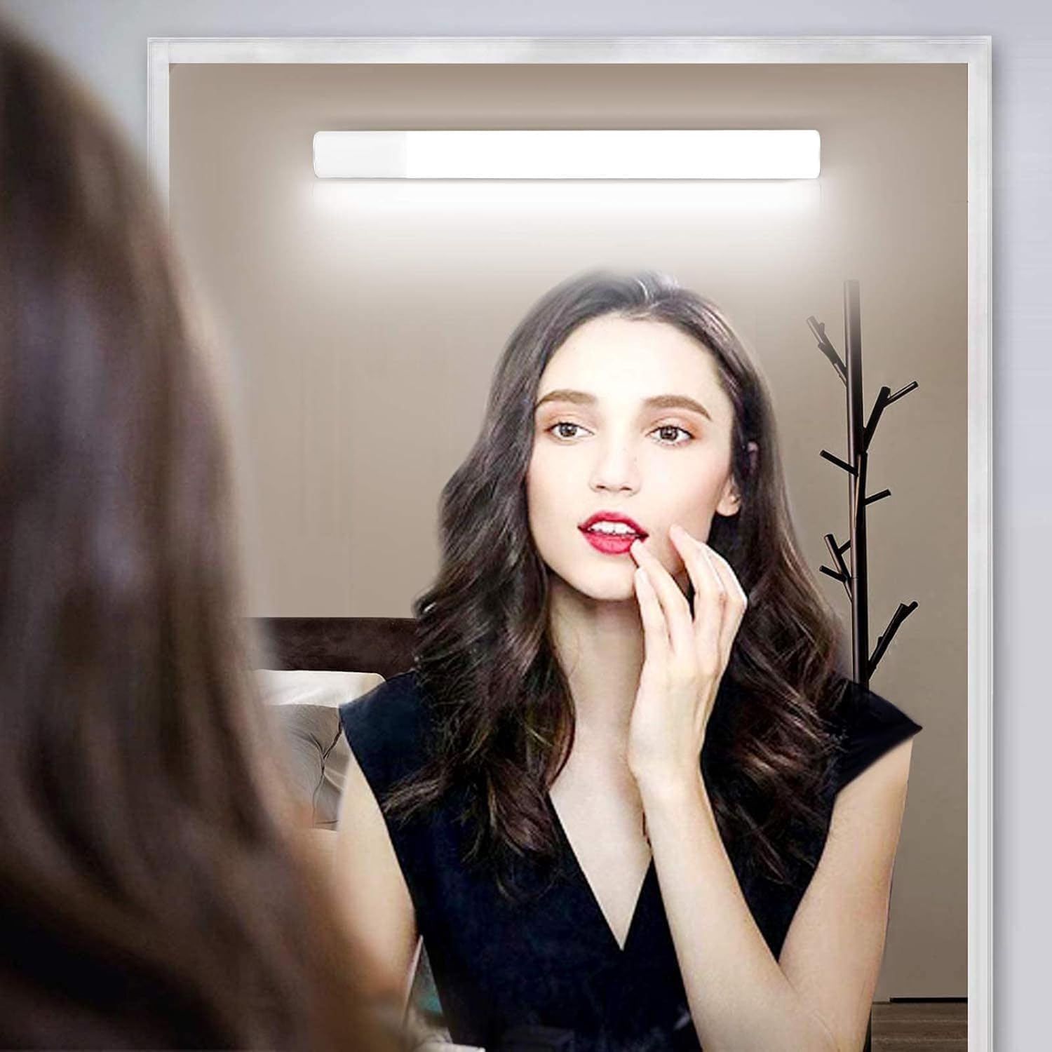 Woman applying lipstick in front of a mirror with a light fixture above.