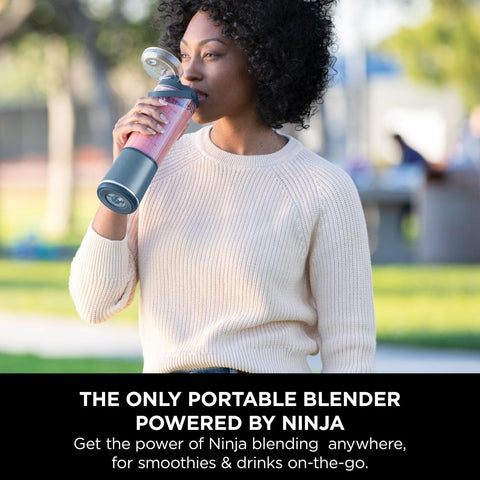 Woman drinking from a portable blender in a park setting