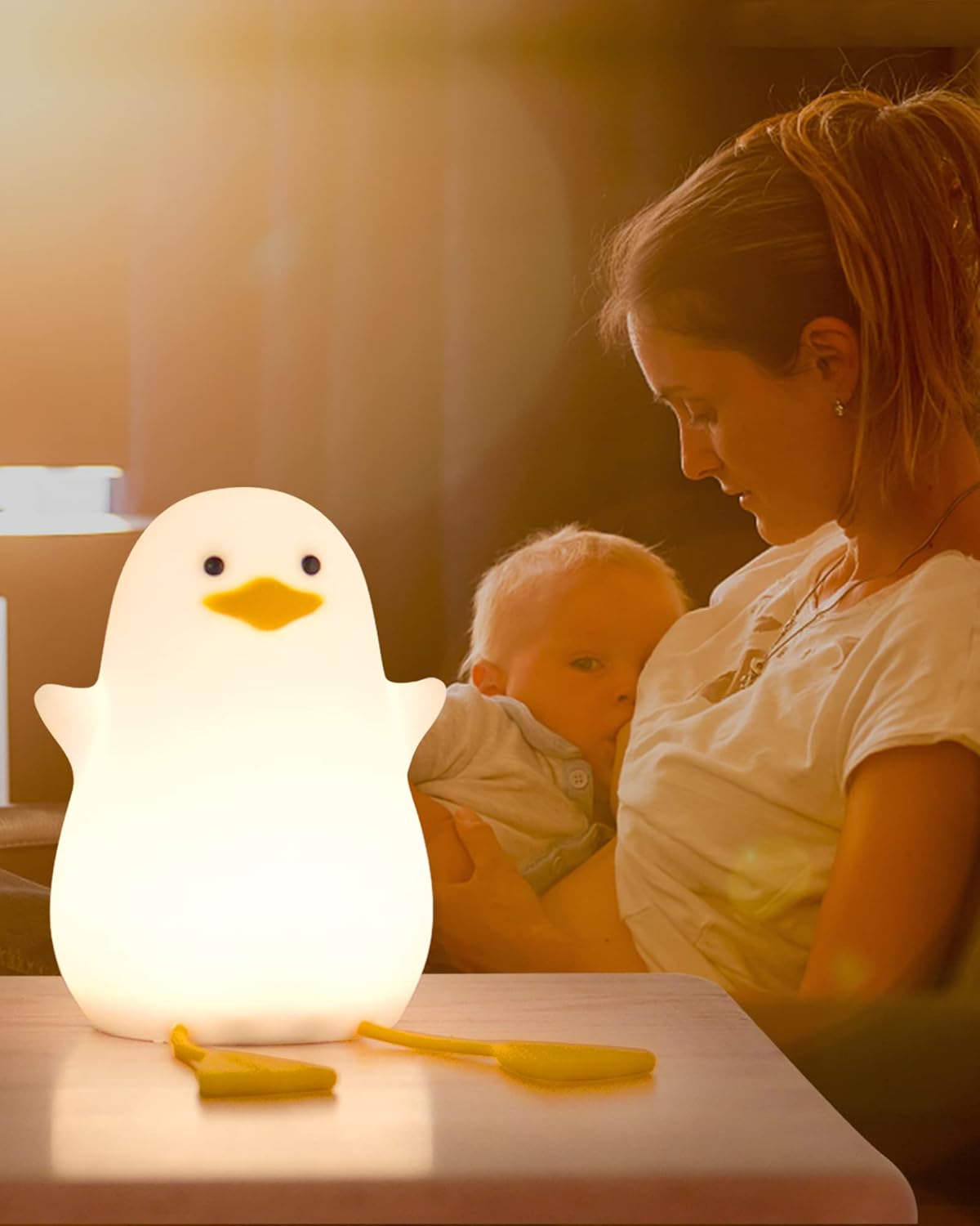 Woman holding a baby next to a glowing duck-shaped night light on a table.