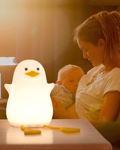Woman holding a baby next to a glowing duck-shaped night light on a table.