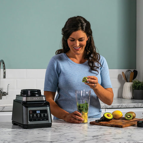 Woman preparing a smoothie with a blender in a kitchen