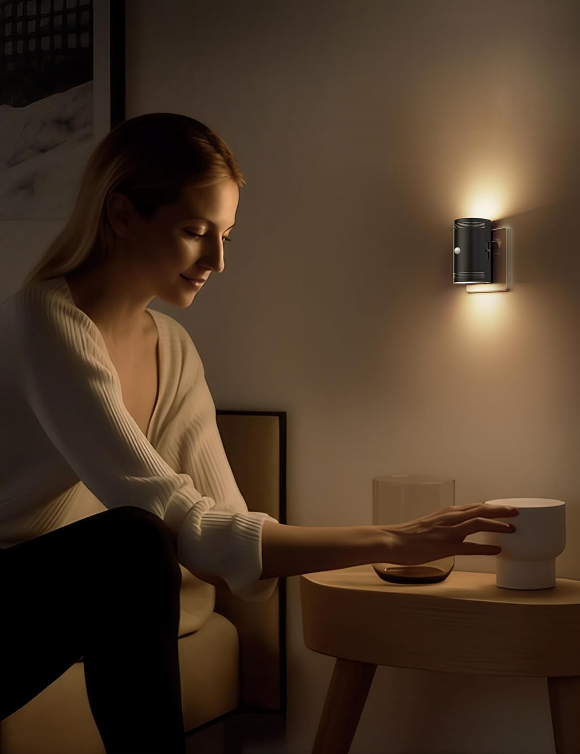 Woman sitting in a dimly lit room with a small table and light fixture.