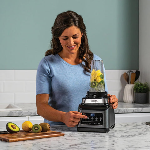 Woman using a Ninja blender with fruits on a kitchen counter