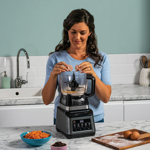 Woman using a blender in a kitchen with ingredients on the counter