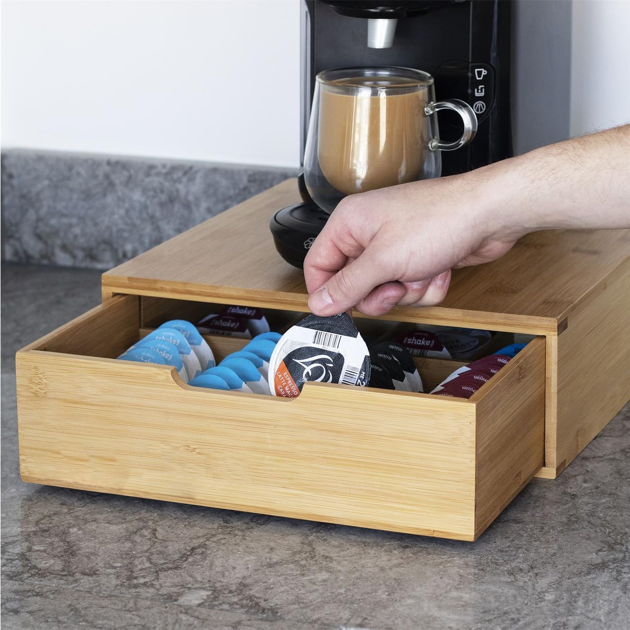 Wooden coffee pod organizer with a hand reaching in to select a pod, placed on a kitchen counter.