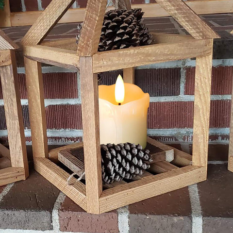 Wooden lantern with a lit candle and pinecones on a brick surface