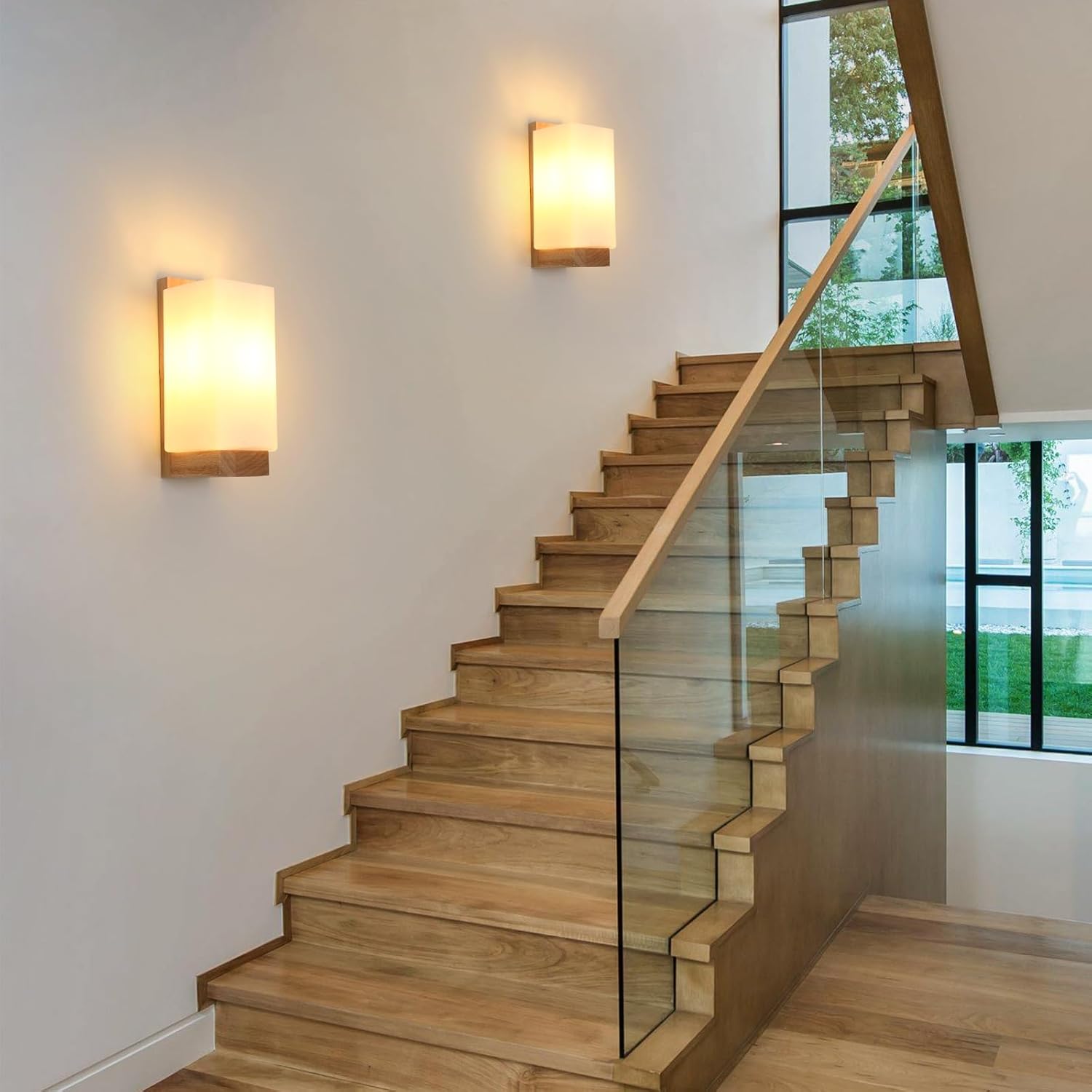 Wooden staircase with glass railings and wall lights in a modern interior setting.