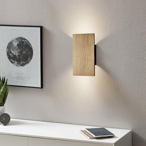 Wooden wall light fixture on a white wall with a framed moon poster and plant.