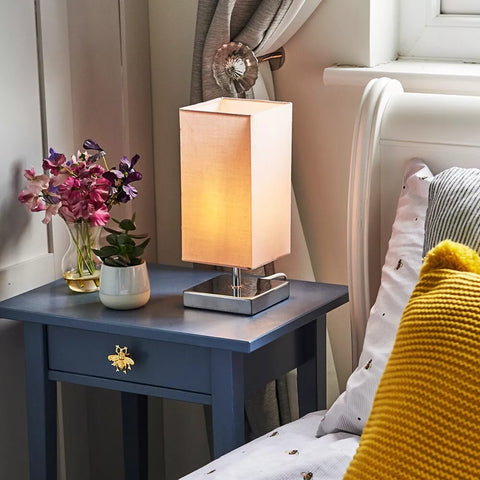 Close-up of the lamp's chrome base and square fabric shade.​

