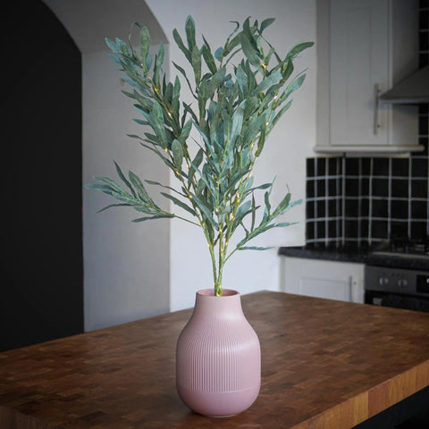 Pink vase with green plant on a wooden table in a kitchen setting