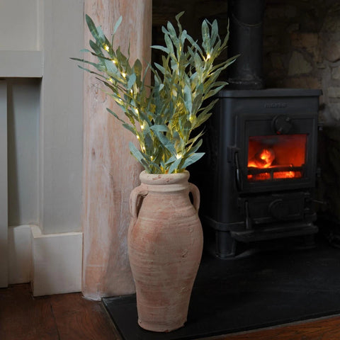 Decorative plant with lights in a terracotta vase in front of a lit wood stove.