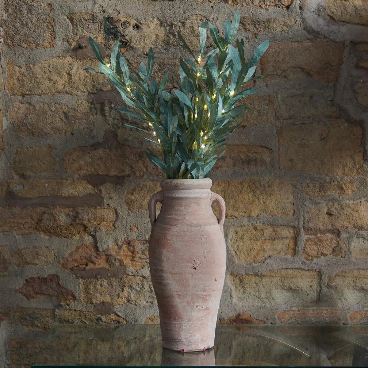 Decorative vase with greenery and lights against a stone wall