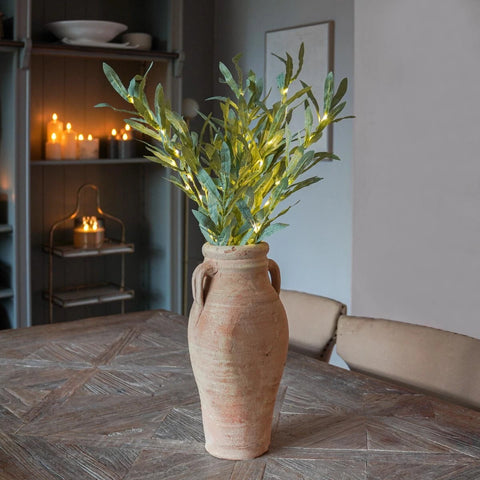 Decorative plant in a terracotta vase on a wooden table with candles in the background.