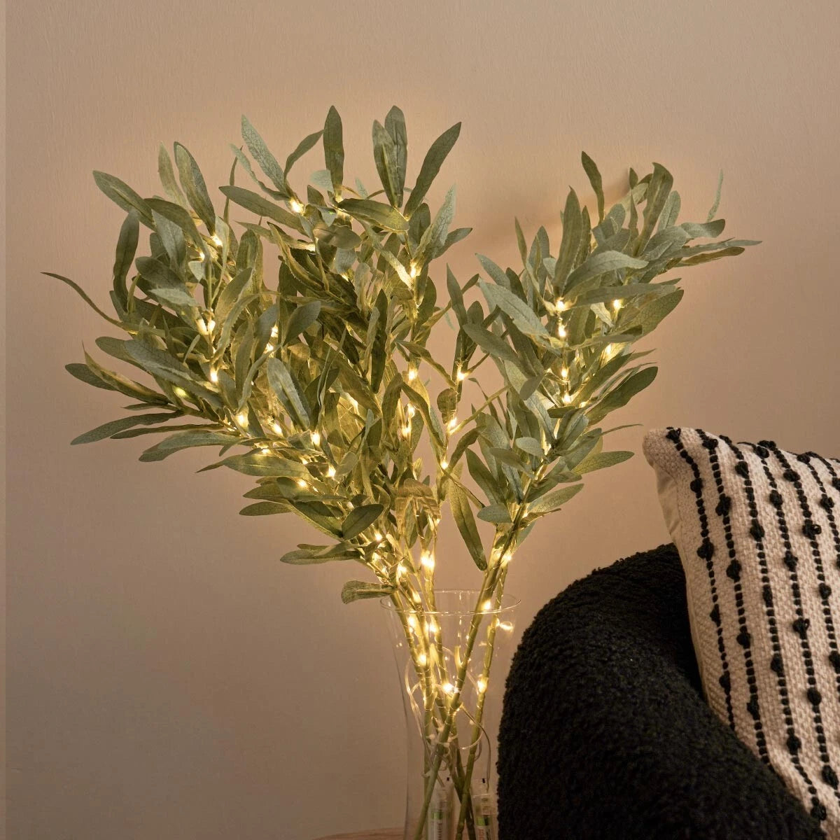 Decorative plant with string lights in a vase against a neutral wall.