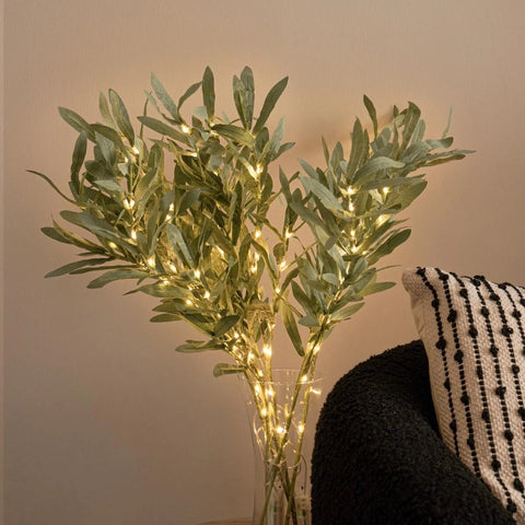 Decorative plant with string lights in a vase against a neutral wall.