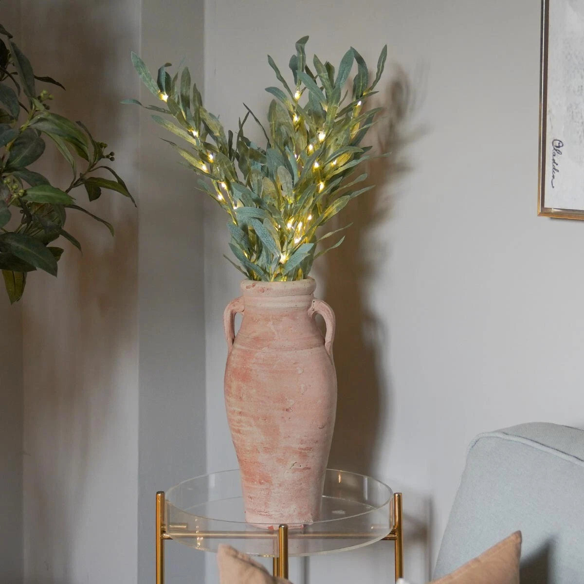 Decorative plant in a pink vase with fairy lights on a glass table against a neutral wall.